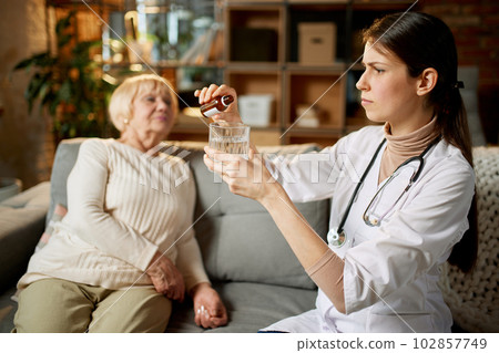 Female doctor dropping meds, drops for her senior female patient sitting on couch. Taking care after health with medicine 102857749