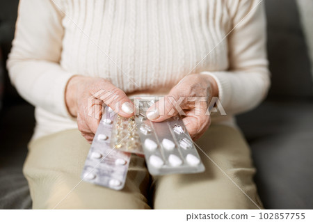 Close-up image of female hands holding pills. Senior woman following her treatment, taking care after health with medical support 102857755