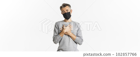 Covid-19, pandemic and social distancing concept. Image of thankful middle-aged man in black medical mask, holding hands on heart and expressing gratitude, standing over white background 102857766
