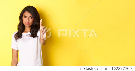 Image of disappointed african-american girl telling no, shaking finger to prohibit or stop someone, disagree with person, standing over yellow background 102857769