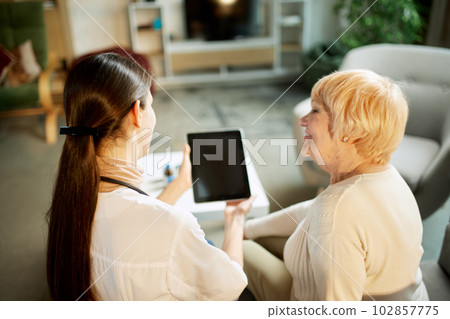 Young woman, doctor using tablet for personal information about patience. Senior woman at appointment on hospital, clinic Young woman, doctor using tablet for personal information about patience. Senior woman at appointment on hospital, clinic 102857775
