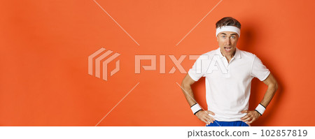 Concept of workout, sports and lifestyle. Portrait of startled middle-aged fitness guy in activewear, drop jaw and looking at camera amazed, standing over orange background Concept of workout, sports and lifestyle. Portrait of startled middle-aged fitness guy in activewear, drop jaw and looking at camera amazed, standing over orange background 102857819
