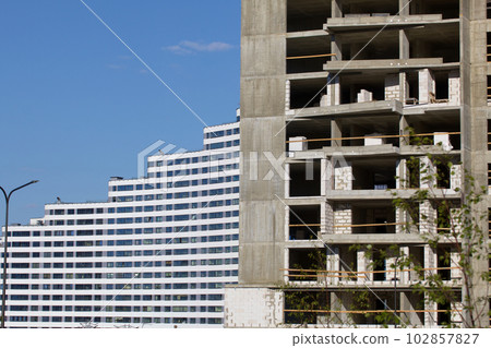 Construction site. Reinforced concrete frames of multi-storey buildings and construction cranes. Finished houses nearby. Against the background of the blue sky. Construction site. Reinforced concrete frames of multi-storey buildings and construction cranes. Finished houses nearby. Against the background of the blue sky. 102857827