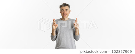 Image of excited and hopeful middle-aged man making a wish, waiting for results, cross fingers for good luck and smiling, standing over white background 102857969