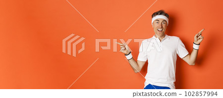 Concept of sport, fitness and lifestyle. Cheerful middle-aged sportsman with headband, smiling happy and pointing fingers sideways, showing left and right copy space 102857994