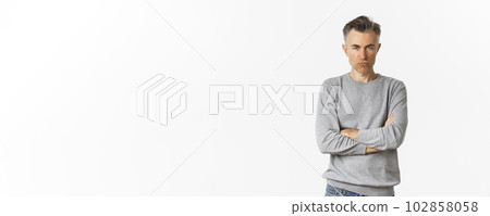 Image of angry middle-aged man feeling offended, cross arms on chest and squinting at camera, standing over white background 102858058