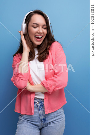 energetic brunette young woman in a shirt and jeans listens to her favorite music on headphones energetic brunette young woman in a shirt and jeans listens to her favorite music on headphones 102858811