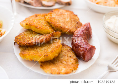 Fried grated potato pancakes with fried sausage on white plate 102859328
