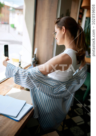 Portrait with young charming girl, blogger taking photo, selfie via smartphone in cafe. Online blogging. Social networks concept Portrait with young charming girl, blogger taking photo, selfie via smartphone in cafe. Online blogging. Social networks concept 102859608