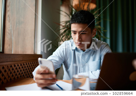 Confident busy male freelancer, businessman doing remote job using smartphone searching information for presentation in cafe 102859664