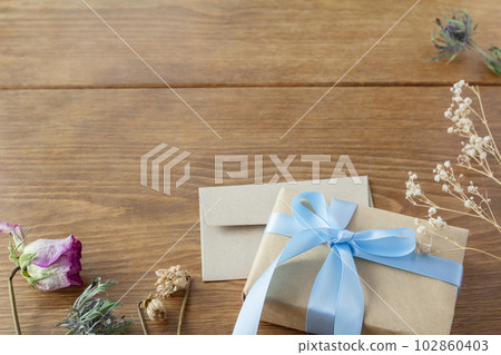 一件帶淡藍色絲帶的禮物和木桌上裝飾著乾花的裝飾框 102860403