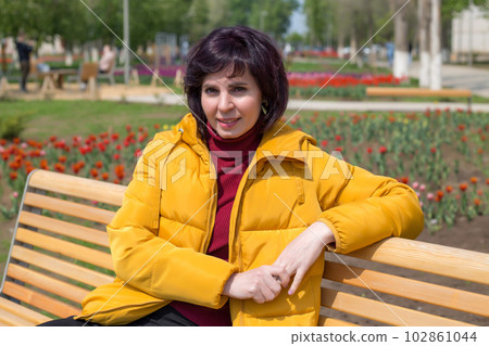 A woman in a yellow jacket sits on a bench among flowers of tulips A woman in a yellow jacket sits on a bench among flowers of tulips 102861044