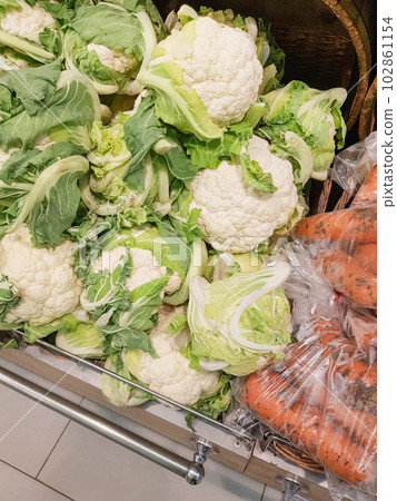 Close-up of cauliflower and fresh raw carrots in plastic bags on the counter in the store. Retail sale of vegetables 102861154