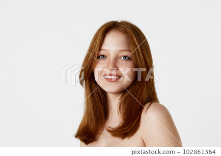 Portrait of young, beautiful, tender redhead girl with well-kept face and straight hair looking at camera against white studio background 102861364