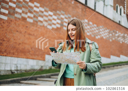 Happy optimistic woman smiling confident holding city map and smartphone at street. Attractive young female tourist is exploring new city. Traveling Europe in spring, old town. Urban lifestyle banner Happy optimistic woman smiling confident holding city map and smartphone at street. Attractive young female tourist is exploring new city. Traveling Europe in spring, old town. Urban lifestyle banner 102861516