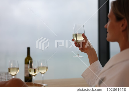 Woman in bathrobe holding glass of white wine closeup Woman in bathrobe holding glass of white wine closeup 102861658