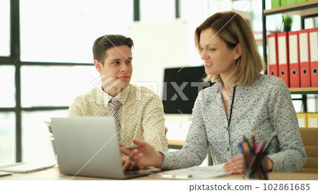 Woman manager teaching trainee how to work on laptop in office 102861685
