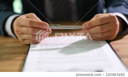 Businessman in suit holding ballpoint pen over document and thinking about signing closeup 102861692