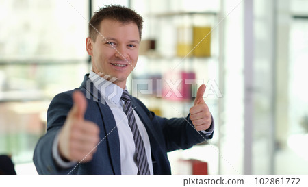 Happy smiling businessman showing thumbs up gesture in office Happy smiling businessman showing thumbs up gesture in office 102861772