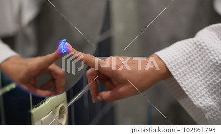 Woman finger pressing blue luminous button on bathroom mirror closeup 102861793