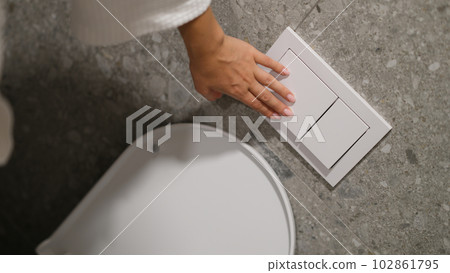 Hand pressing button to drain water in toilet bowl in restroom closeup 102861795