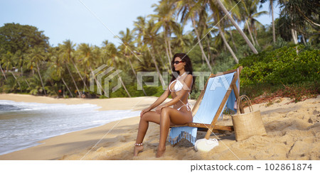 Banner Holiday Photo of Tanned Woman in White Bikini on a Beach Chair 102861874