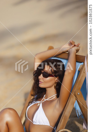 Fashion Holiday Photo of Tanned Woman in Chic White Bikini on a Beach Chair 102861875