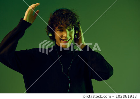 Man wearing headphones listening to music, dancing and singing, DJ teenager happiness and smile, hipster lifestyle, portrait green background mixed neon light, copy space Man wearing headphones listening to music, dancing and singing, DJ teenager happiness and smile, hipster lifestyle, portrait green background mixed neon light, copy space 102861918