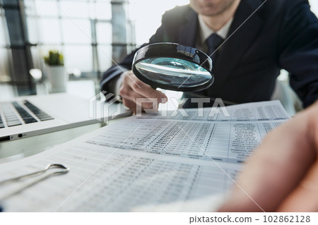 Businessman looking through a magnifying glass to document Businessman looking through a magnifying glass to document 102862128