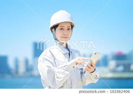A woman in work clothes holding a smartphone A woman in work clothes holding a smartphone 102862406