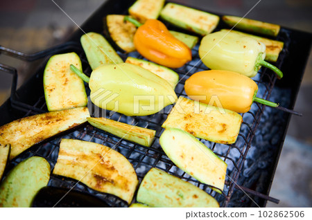 Close-up of fresh marinated seasoned bell peppers and slices of zucchini grilling on grate over charcoals in the barbecue grill. BBQ party. Preparing delicious food outdoor. Weekend leisures. Picnic Close-up of fresh marinated seasoned bell peppers and slices of zucchini grilling on grate over charcoals in the barbecue grill. BBQ party. Preparing delicious food outdoor. Weekend leisures. Picnic 102862506
