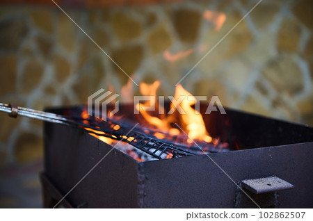 Empty flaming charcoal grill with open fire, ready for product placement. Concept of summer grilling, barbecue, bbq and party. Selective focus. Close-up Empty flaming charcoal grill with open fire, ready for product placement. Concept of summer grilling, barbecue, bbq and party. Selective focus. Close-up 102862507