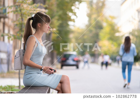 Young woman sitting alone on city street outdoors waiting for someone to arrive. Arriving late on business meeting concept 102862778