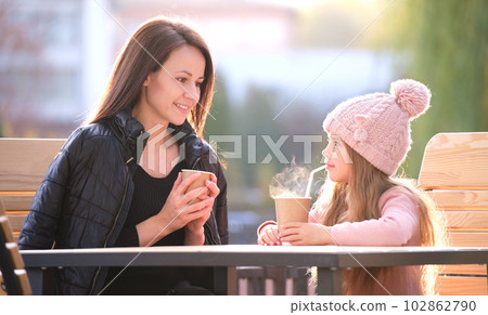 Young mother and her child daughter having good time together sitting at street cafe with hot drinks on sunny fall day. Happiness in family relations concept 102862790