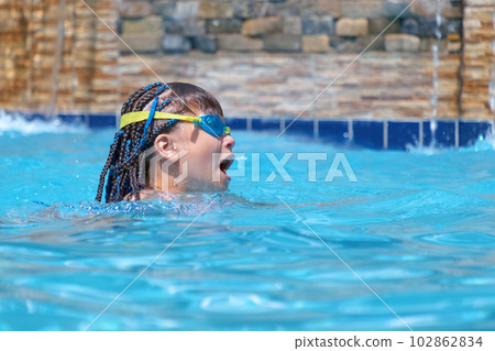 Young child girl in goggles exercises swimming in blue pool water. Summer recreation activity concept Young child girl in goggles exercises swimming in blue pool water. Summer recreation activity concept 102862834