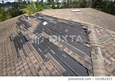 Wind damaged house roof with missing asphalt shingles after hurricane Ian in Florida. Repair of home rooftop concept Wind damaged house roof with missing asphalt shingles after hurricane Ian in Florida. Repair of home rooftop concept 102862853