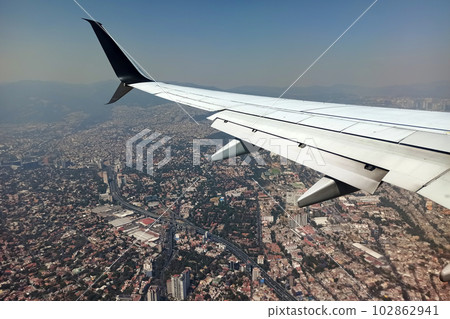 View on Mexico city through airplane window of commercial jet plane landing in local airport. Air travelling concept View on Mexico city through airplane window of commercial jet plane landing in local airport. Air travelling concept 102862941