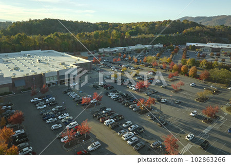 Top view of many cars parked on a parking lot in front of a strip mall plaza. Concept of consumerism and market economy 102863266