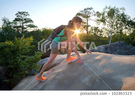 Sportive woman climbing alone on hillside rocky trail. Female hiker overcoming difficult cliff on wilderness path. Active lifestyle concept 102863323
