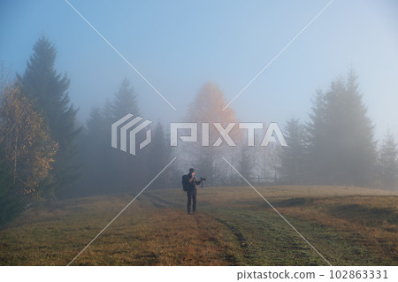 Small figure of lonely hiker enjoying his time on wild forest trail on foggy autumn day 102863331