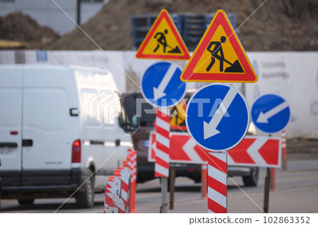 Roadworks warning traffic signs of construction work on city street and slowly moving cars Roadworks warning traffic signs of construction work on city street and slowly moving cars 102863352
