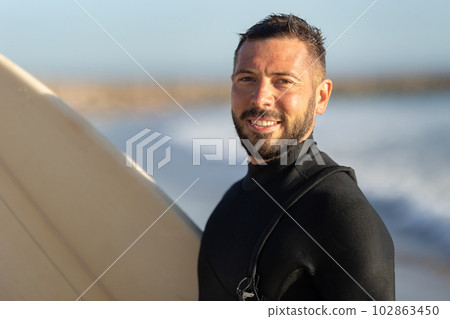 Smiling man surfer in a wetsuit looking in the camera 102863450