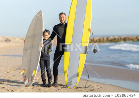 A family of surfers - smiling father and son standing on the seashore with their surfing boards 102863454