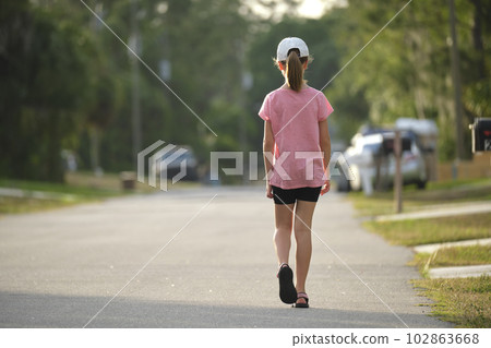Rear view of confident young child girl walking along the sunny alley. Active lifestyle on summer holidays Rear view of confident young child girl walking along the sunny alley. Active lifestyle on summer holidays 102863668