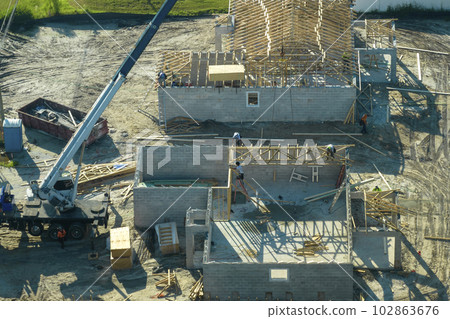 Professional builders and crane truck working on roof construction of unfinished suburban home with wooden frame structure in Florida rural area. Concept of housing development in America 102863676