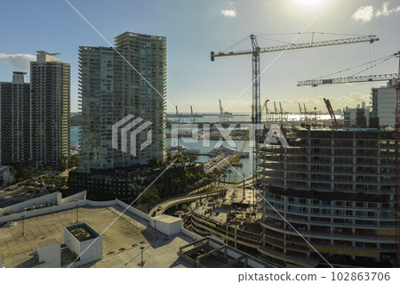 New construction site of developing residense in american urban area. Industrial tower lifting cranes in Miami, Florida. Concept of housing growth in the USA New construction site of developing residense in american urban area. Industrial tower lifting cranes in Miami, Florida. Concept of housing growth in the USA 102863706