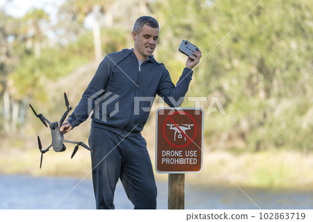 Man is sad that he is not allowed to fly his quadcopter state park no drone area. Operator is unauthorised to use UAS near restriction sign 102863719