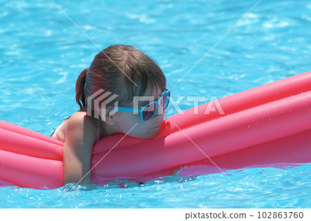 Happy child girl relaxing on inflatable air mattress in swimming pool on sunny summer day during tropical vacations. Summertime activities concept Happy child girl relaxing on inflatable air mattress in swimming pool on sunny summer day during tropical vacations. Summertime activities concept 102863760
