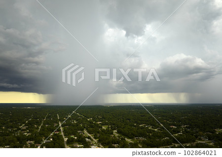 Dark stormy clouds forming on gloomy sky during heavy rainfall season over suburban town area 102864021