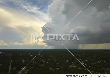 Dark stormy clouds forming on gloomy sky during heavy rainfall season over suburban town area Dark stormy clouds forming on gloomy sky during heavy rainfall season over suburban town area 102864022